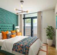 Modern bedroom with a teal accent wall, double bed with colorful linens, two wooden nightstands, a potted plant, abstract art, and a large window with curtains.