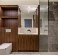 Modern bathroom with a glass-enclosed shower on the right, a wall-mounted toilet on the left, and a wooden cabinet and basin in the center.
