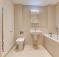 Modern bathroom with beige tiles featuring a wall-mounted toilet, sink, and bathtub. A mirror is above the sink, and a towel rail is on the left wall.
