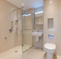 Modern bathroom with beige tiles, featuring a glass shower enclosure, wall-mounted sink, and toilet.
