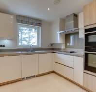 Modern kitchen with light cabinets, built-in ovens, a stovetop, and a window. Neutral tones and minimalistic design create a clean, spacious look.
