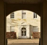An arched brick passageway frames a view of a white building facade. The entrance has a white door with rectangular windows on either side and "Scott Polar Institute" above it.