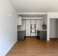 Modern kitchen with white cabinets, dark countertops, built-in appliances, and wooden flooring in an open space layout.