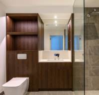 Modern bathroom with a wall-mounted toilet, wooden cabinetry, large mirror, and a glass-enclosed shower with gray tiles.