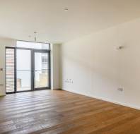Empty room with wooden floors, off-white walls, ceiling light, and a glass door flanked by windows leading to a small balcony.