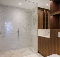 Modern bathroom with a glass-enclosed shower, marble tiles, wooden cabinetry, and a rectangular sink.