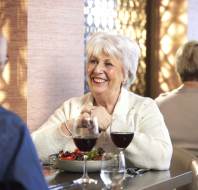 Elderly woman smiling at a man while sitting at a table with a salad and red wine.
