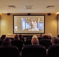 People seated in a small theater watching a movie on a large screen.