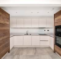 Modern kitchen with white cabinets, wood paneling, built-in oven, and stovetop. Light gray tile flooring complements the minimalist design.