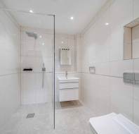 Modern bathroom with beige tiled walls and floor, featuring a glass-enclosed shower, wall-mounted toilet, and a vanity with a sink and mirror.