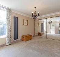 Room with large mirrored closet doors, a window with curtains, a chandelier, wall radiator, and a wooden box. A small shelf holds decorative items.