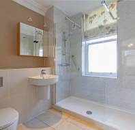Modern bathroom with a glass-enclosed shower, wall-mounted sink, toilet, and mirror cabinet. Beige tiles and a towel radiator are present.