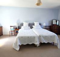 A bedroom with two single beds pushed together, light blue walls, wooden furniture, a TV, and a window allowing natural light into the room.
