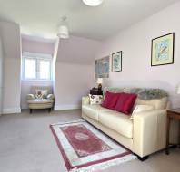 A cozy living area with a cream sofa, red and white pillows, a bookshelf, an armchair by the window, and framed art on light-colored walls.
