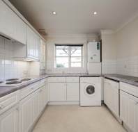 A clean, white kitchen with tiled backsplash, electric stove, washing machine, gray countertops, and a window above the sink.