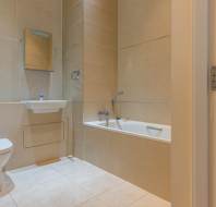 A modern bathroom with beige tiles, featuring a toilet, wall-mounted sink with mirror, and a bathtub with a handheld showerhead.