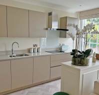 Modern kitchen with beige cabinets, built-in oven, electric cooktop, sink, and decorative orchids on a white counter near a large window with garden view.