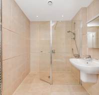 Modern bathroom with beige tiles, a wall-mounted sink, a glass-enclosed shower, and a metal towel radiator.