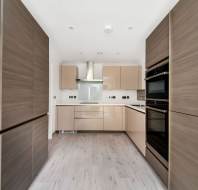 Modern kitchen with light wood cabinets, white countertops, and stainless steel appliances including an oven and extractor hood. The floor is light wood, and the walls are white.