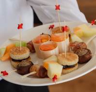 A plate of assorted appetizers including skewered melon, stuffed mushrooms, smoked salmon cups, and small meat patties.