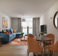 Modern living room with a blue sofa, colorful rug, and orange dining chairs. A round mirror hangs on the wall, and a TV is opposite the sofa. Large window with curtains in the background.