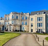 Large white historic mansion with multiple windows and balconies, set against a clear blue sky, surrounded by well-kept lawns and a curved driveway.