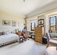 A cozy room with a bed, desk, and wooden furniture. Framed pictures adorn the walls. The window offers a view of fields.