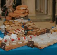 A market stall with various pastries, cakes, pies, and loaves of bread displayed on a blue tablecloth, each with handwritten price tags.
