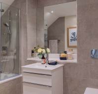 Modern bathroom with a bathtub, glass shower screen, and a wall-mounted showerhead. White vanity with a mirror above, and decorative items including flowers and toiletries on the counter.