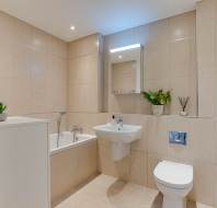 Modern bathroom with beige tiled walls, white bathtub, wall-mounted sink, toilet, mirrored cabinet, towel radiator, and potted plants for decoration.