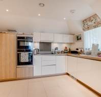 Modern kitchen with white cabinets, built-in oven, and various small appliances on the countertops; a window with a floral blind lets in natural light.