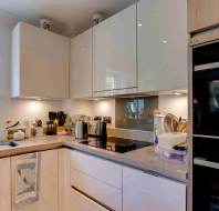 Modern kitchen with white cabinets, electric stove, built-in oven, sink, kettle, and utensils on the countertop near a window with a plant.
