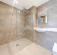 Modern bathroom with beige tiles, a glass walk-in shower, wall-mounted sink with mirror, and a toilet.