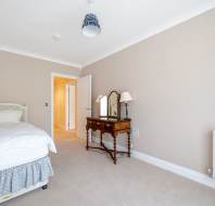 A tidy bedroom with a single bed, a wooden vanity with mirrors, beige walls, a white door, and a radiator on a carpeted floor.