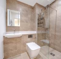 Modern bathroom with beige tile walls, wall-mounted sink, floating toilet, glass-enclosed shower, and metal towel radiator on the left.