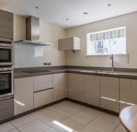 Modern kitchen with neutral cabinets, built-in oven and microwave, ceramic cooktop, large countertop, window above the sink, and round wooden table in the foreground.
