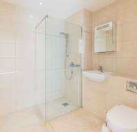 Modern bathroom with beige tiled walls, glass-enclosed walk-in shower, wall-mounted sink, mirror, and toilet.