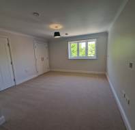 Empty, carpeted room with light-colored walls, a ceiling light, two closets with white doors, and a window letting in daylight.