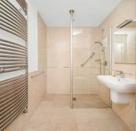 Modern accessible bathroom with beige tiles, a walk-in shower with grab bars, a wall-mounted sink, and a heated towel rail.