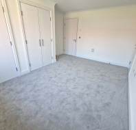 Empty room with light gray carpet, white walls, two built-in double-door wardrobes, and a closed white door.