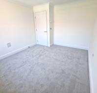 Empty room with light grey carpet, white walls, a closed white door, and electrical outlets on the lower parts of the walls.