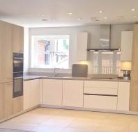 Modern kitchen with light wood and white cabinets, built-in appliances, under-cabinet lighting, and a window above the sink.