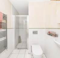 Modern bathroom with a walk-in shower, wall-mounted toilet, sink, heated towel rail with a pink towel, and a mirrored cabinet above the sink.