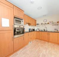 Spacious kitchen with light wood cabinets, built-in oven and microwave, sink, countertop appliances, tiled backsplash, and wall clock.