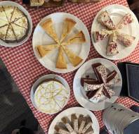 A variety of sliced cakes and breads are displayed on white plates atop a red and white checkered tablecloth.