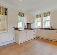 Modern kitchen with white cabinets, brown countertops, tiled floor, stainless steel appliances, and multiple windows with striped Roman shades.