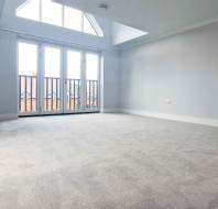Empty, carpeted room with light grey walls, a large window with glass doors leading to a small balcony, and a triangular transom window above.