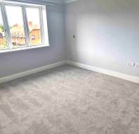 Empty room with light grey walls, beige carpet, a white door, and a window overlooking neighboring houses.