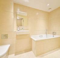 Modern bathroom with beige tiles, a wall-mounted toilet, a small sink with a mirror above, a built-in bathtub, and a heated towel rail.