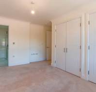 Empty room with beige carpet, white walls, two closed double-door closets, an open door leading to a bathroom, and a ceiling light fixture.